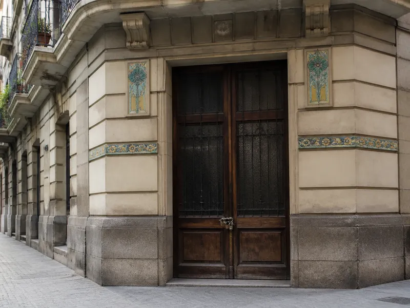 Portal residencial de Les Corts en Barcelona, puerta de finca y cerradura, calle ancha sin rostros.