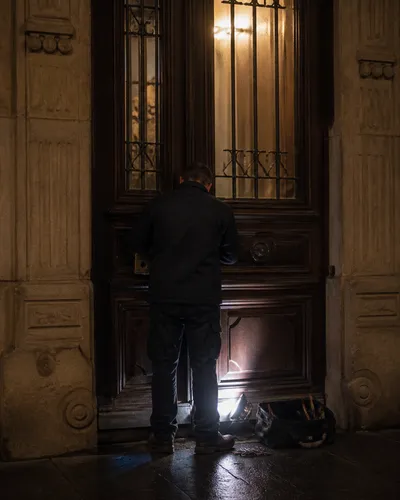 Locksmith from behind with a work lamp at a residential doorway, no face visible.