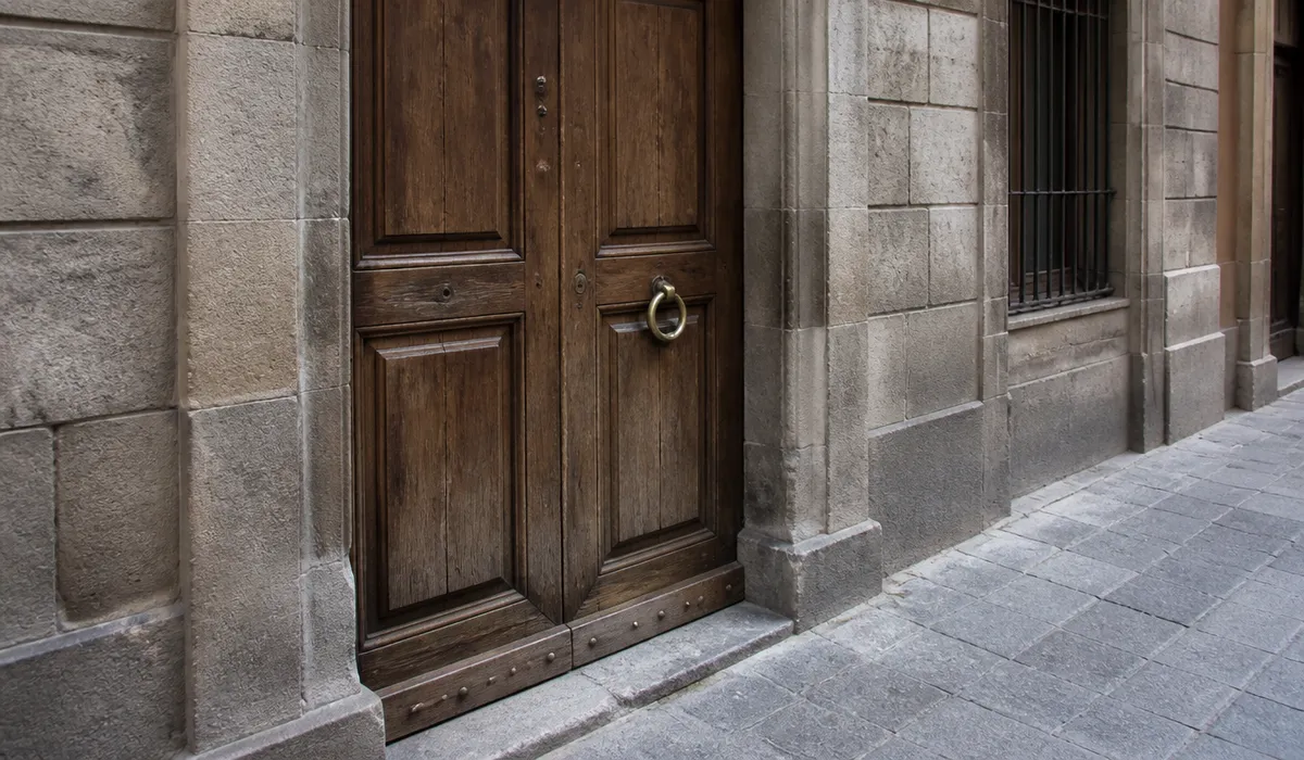 Residential portal in Barcelona with a wooden door and lock, empty pavement, no faces.